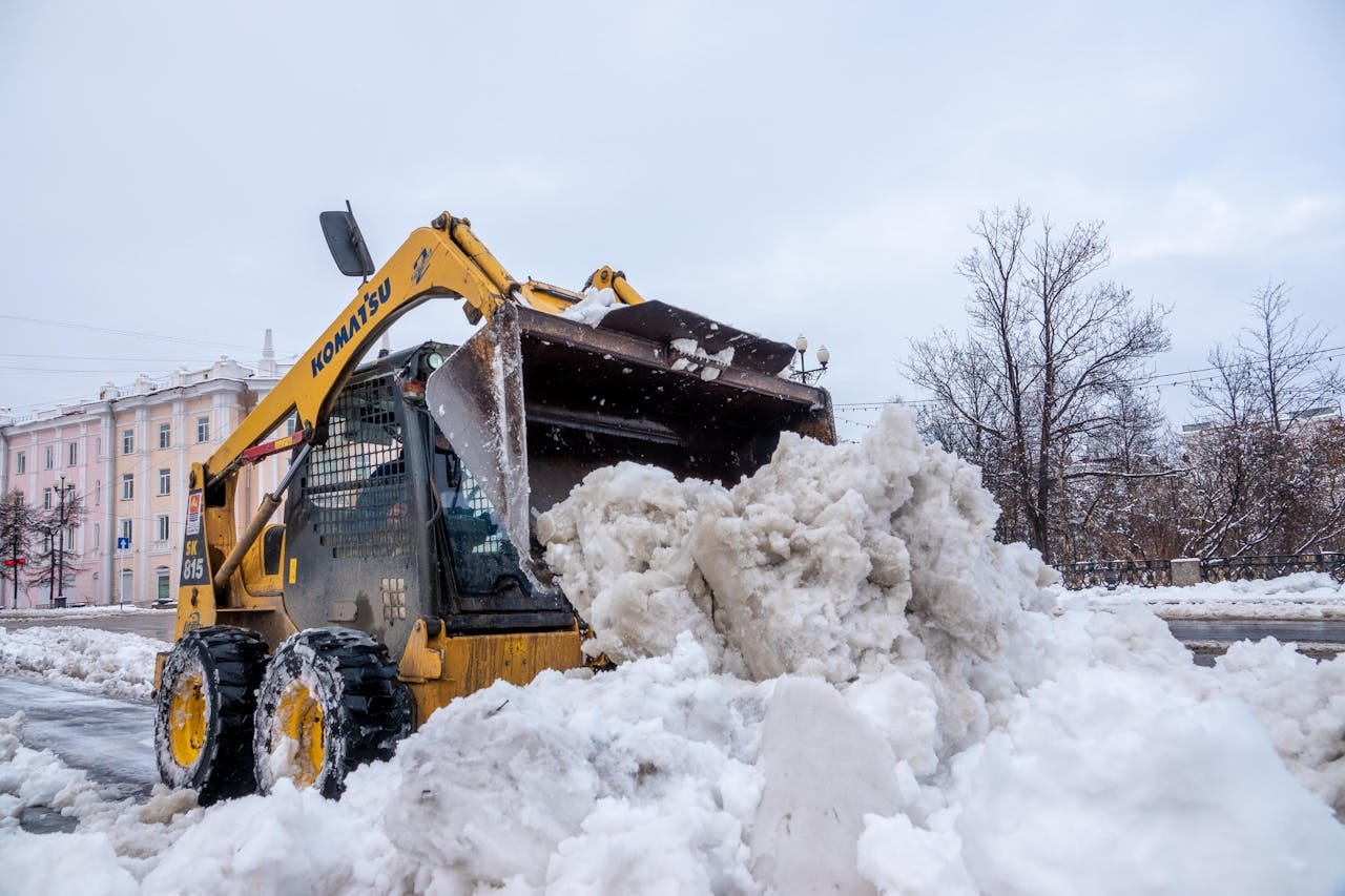 A yellow tractor clears snow on a city street after a winter snowstorm, showcasing urban cleanup.